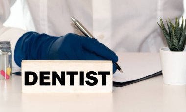 Tıbbi, dişçi konsepti. Metin küplerin üzerinde yazıyor, DENTIST. Arka planda, küplerinde diş fırçası olan bir çene modeli var. Diş hastalıklarının önlenmesi.