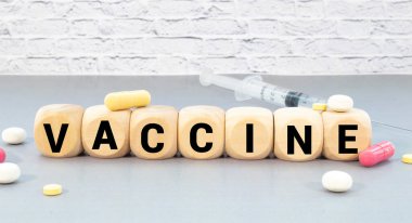 Ağaç bloğunda yüz maskesi ve el dezenfektanı ile yazılmış VACCINE kelimesi. Tahta masadaki yazı, Wuhan Coronavirus aşısı..