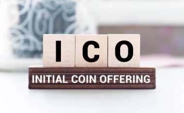 ICO kısaltması, ahşap bloklarda sunulan ilk madeni para, sarı arka plan. Kripto para birimleri kavramı.