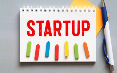 STARTUP kelimesi tahta bir arka planda, bir kalem ve gözlüğün yanındaki tahta küplere yazılmıştır.