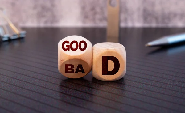 Good or bad symbol. Businessman hand turns a cube and changes the word 'bad' to 'good'. Beautiful yellow table, white background, copy space. Business and bad or good concept.