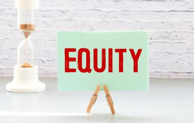 Küçük karatahta üzerinde Word Equity ve kavanozdaki bulanık arkaplanlı kitaplar, yeşil bitki ve saat. Mali Konsept.