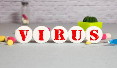 Masadaki tahta bloklardaki VIRUS kelimesi. Arka planda haplar, vitaminler, steteskop ve şırınga ile tıbbi konsept