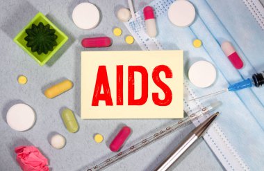 AİDS kelimesi beyaz bir not defterine steteskop, şırınga, elektronik termometre ve hapların yanında mavi bir arkaplan üzerine yazılmış. Tıbbi konsept