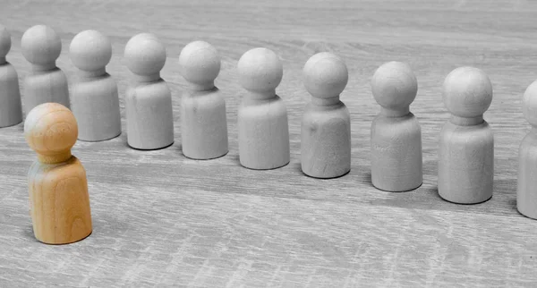 Abstract wooden figures of man and people stand apart from each other behind him on blue background.