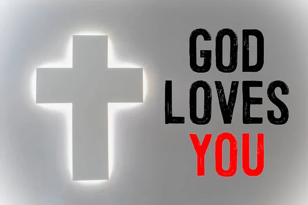 Text Bůh vás miluje, koncept a bílý kříž se světlem kolem okrajů — Stock fotografie