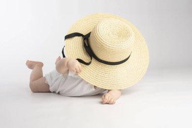 Beyaz arka planda, büyük hasır şapkalı şirin bir bebek.