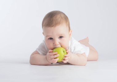 Beyaz arka planda yeşil elma yiyen şirin bir bebek.