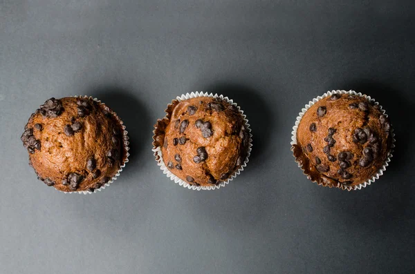 Três muffins de chocolate em um fundo escuro — Fotografia de Stock