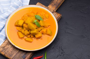 Siyah arkaplanda seramik bir tabakta servis edilen köri ya da balkabağı çorbası - mesaj yazmak için alan ile üst görünüm.