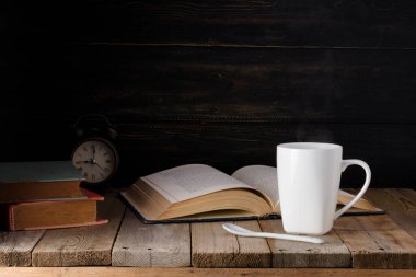 Siyah kahve fincanı ve eski kitaplar ve eski ahşap bir masa ve siyah tahta bir duvarın üzerindeki saat..