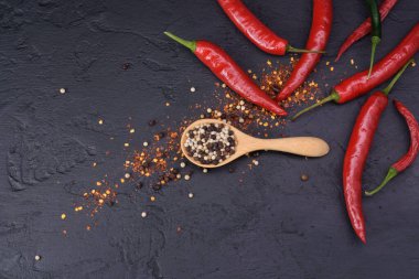 Siyah bir masaya yerleştirilmiş parlak kırmızı biberlerle ahşap bir kaşıkta siyah ve beyaz biber.