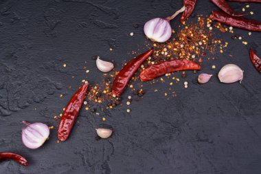 Kırmızı biberli ve biberli soğanlı sarımsak siyah masaya saçılmış. Mesaj yazmak için yer var..