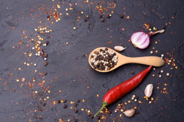 Ahşap kaşıkta biber ve siyah masaya saçılmış kırmızı biberli soğan sarımsağı. Mesaj yazmak için yer var..