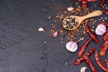 Ahşap kaşıkta biber ve siyah masaya saçılmış kırmızı biberli soğan sarımsağı. Mesaj yazmak için yer var..