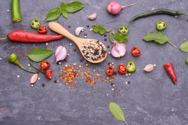 Ahşap bir kaşıkta biber kırmızı biber fesleğen sarımsak ve siyah ahşap bir masaya yerleştirilmiş baharatlar..