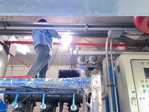 机修工站在脚手架焊管上修理泵房的洒水系统 — 图库照片