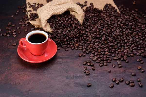 Red coffee cup with black needle coffee with saucer and fragrant roasted coffee beans on the needle colored table - top view with copy space.