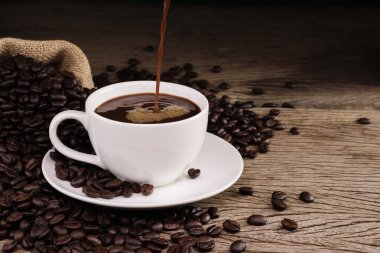 Çok sayıda sade kahve ve kavrulmuş kahve çekirdekleri ile birlikte beyaz bir kahve fincanı sıcak bir atmosferde ahşap bir masanın etrafına serilmiştir. Fotokopi alanı olan koyu bir arkaplanda