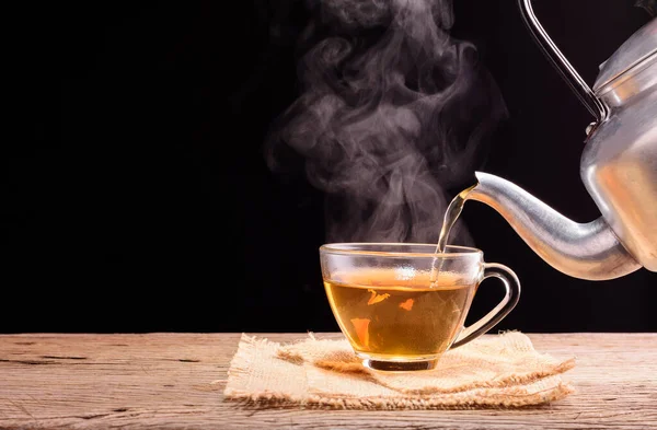 Çay seremonisi çay seremonisi taze demlenmiş bir fincan siyah çay ahşap bir masaya konur ılık, yumuşak bir ışığın siyah bir arka plana doğru parladığı yere..