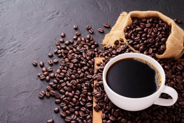 Siyah kahve fincanı ve koyu arkaplanda taze kavrulmuş kahve çekirdekleri. en üstteki görünüm.