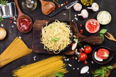 İştah açıcı klasik İtalyan spagettisi domates soslu siyah bir tabakta servis edilir. Sarımsak, soğan ve fesleğenli koyu siyah masa üzerinde çatal - üst görünüm