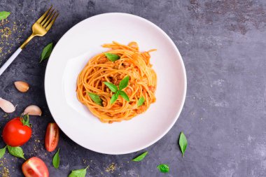 Ağız sulandıran beyaz tabakta klasik İtalyan spagetti makarnası. Ketçap ve fesleğen, sarımsak, domates, ahşap masa çatalı - üst görünüm