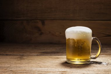 Beyaz bira köpüklü bira bardağı, siyah ahşap masa arkasında.