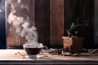 Bir fincanda sade kahve, kavrulmuş kahve çekirdekleri ve bir öğütücü sabah atmosferinde masanın üzerinde, siyah ahşap duvarların önünde..