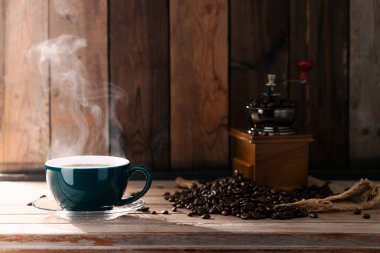 Yeşil bardakta sade kahve, kavrulmuş kahve çekirdekleri ve bir öğütücü ile birlikte sabah güneşinin altında..