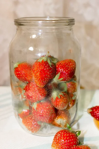  Kırmızı çilekler masanın üstünde ve cam bir kavanozun içinde.