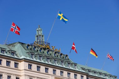 Stockholm, İsveç - 31 Temmuz 2020: Açık mavi gökyüzüne karşı Norveç, İsveç, Danimarka, Almanya ve Büyük Britanya 'yı temsil eden bayrağıyla Grand Hotel' in en üst katları.