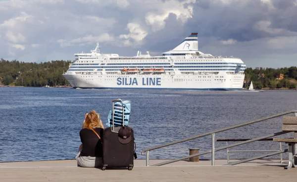 Lidingo, İsveç - 4 Temmuz 2016: Bir kadın rıhtımda oturmuş, valiziyle birlikte gün ışığında, Silja Line feribotunun Helsinki 'ye geçişini bekliyor..