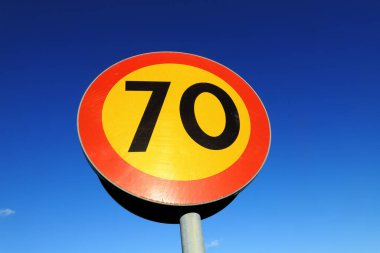 Düşük açılı daire görüntüsü sarı 70 hız sınırı işareti ve kırmızı kenarlı mavi gökyüzü.