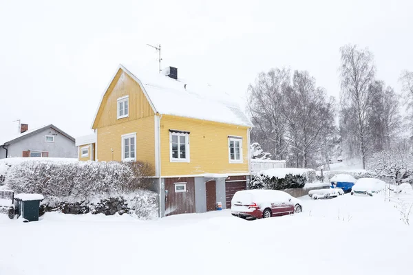 Yellow Swedish two-story single family house with a broken roof constructed in the late 1940s during snowfall in the winter season.