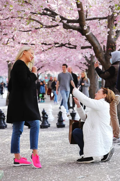 2021年4月30日 瑞典斯德哥尔摩 一位金发碧眼的年轻女子向另一位女子摆姿势 这名女子在繁茂的日本樱桃树下给她拍照 — 图库照片