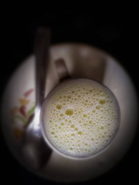 Baloncuklu süt dolu bir bardak. Koyu arkaplanda bulanık kaşık tabağı