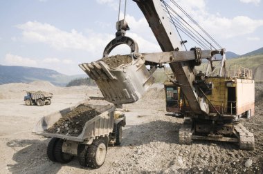 Çöp kamyonu ve kazıcı iş başında. Madencilik. Kazıcı, bir çöp kamyonunun cesedine dağ toprağı yüklüyor.