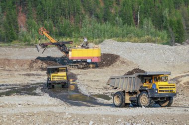 Çöp kamyonu ve kazıcı iş başında. Madencilik. Kazıcı, bir çöp kamyonunun cesedine dağ toprağı yüklüyor.