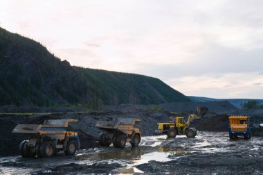 Çöp kamyonu ve ön yükleyici çalışıyor. Madencilik. Bir tekerlek yükleyicisi, bir çöp kamyonunun cesedine dağ toprağı yüklüyor..