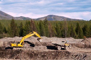 Çöp kamyonu ve kazıcı iş başında. Madencilik. Kazıcı, bir çöp kamyonunun cesedine dağ toprağı yüklüyor.