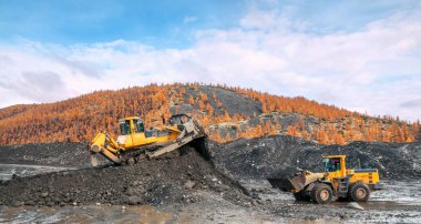 Buldozerler ve tekerlek yükleyiciler iş başında. Madencilik. Buldozerler dağlık ormanlardaki toprağı kesiyor ve tekerlek yükleyicileri toprağı taşıyor.