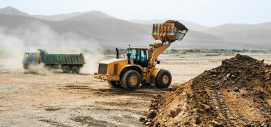 Dağlık bir bölgede, bir yaz gününde toprak işleri. Tekerlek yükleyiciler, buldozerler ve çöp kamyonları çalışıyor. Bu toprağı taşıyan çöp kamyonlarının tozu.