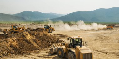 Dağlık bir bölgede, bir yaz gününde toprak işleri. Tekerlek yükleyiciler, buldozerler ve çöp kamyonları çalışıyor. Bu toprağı taşıyan çöp kamyonlarının tozu.