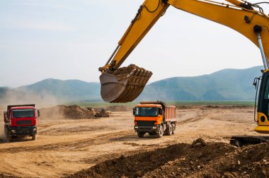 Kazı kovası, çöp kamyonlarının arka planına karşı. Toprak işleri, yükleme ve boşaltma.