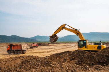 Kazı kovası, çöp kamyonlarının arka planına karşı. Toprak işleri, yükleme ve boşaltma.