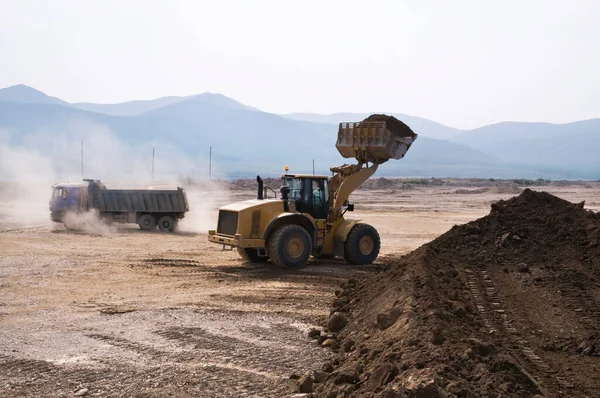 Earthworks on a summer day in a mountainous area. Wheel loaders, bulldozers and dump trucks are in operation. Dust from dump trucks that transport this soil