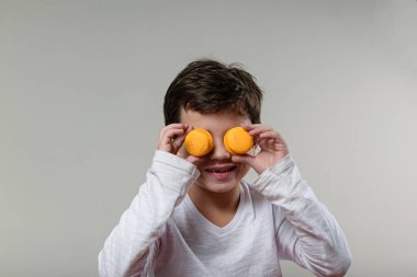 6 yaşında bir çocuk, gülümsüyor ve gözlerine 2 badem kurabiyesi koyuyor..