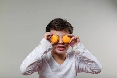 6 yaşında bir çocuk, gülümsüyor ve gözlerine 2 sarı badem kurabiyesi koyuyor..