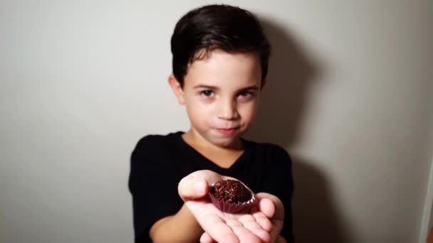 Criança de 7 anos mostrando um doce, comendo um brigadeiro e saindo. — Vídeo de Stock